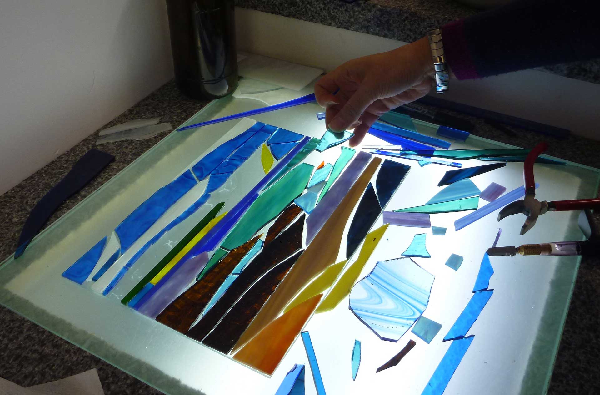 A customer creates a beautiful picture from pieces of glass before glueing them to the backing glass and then grouting the finished design