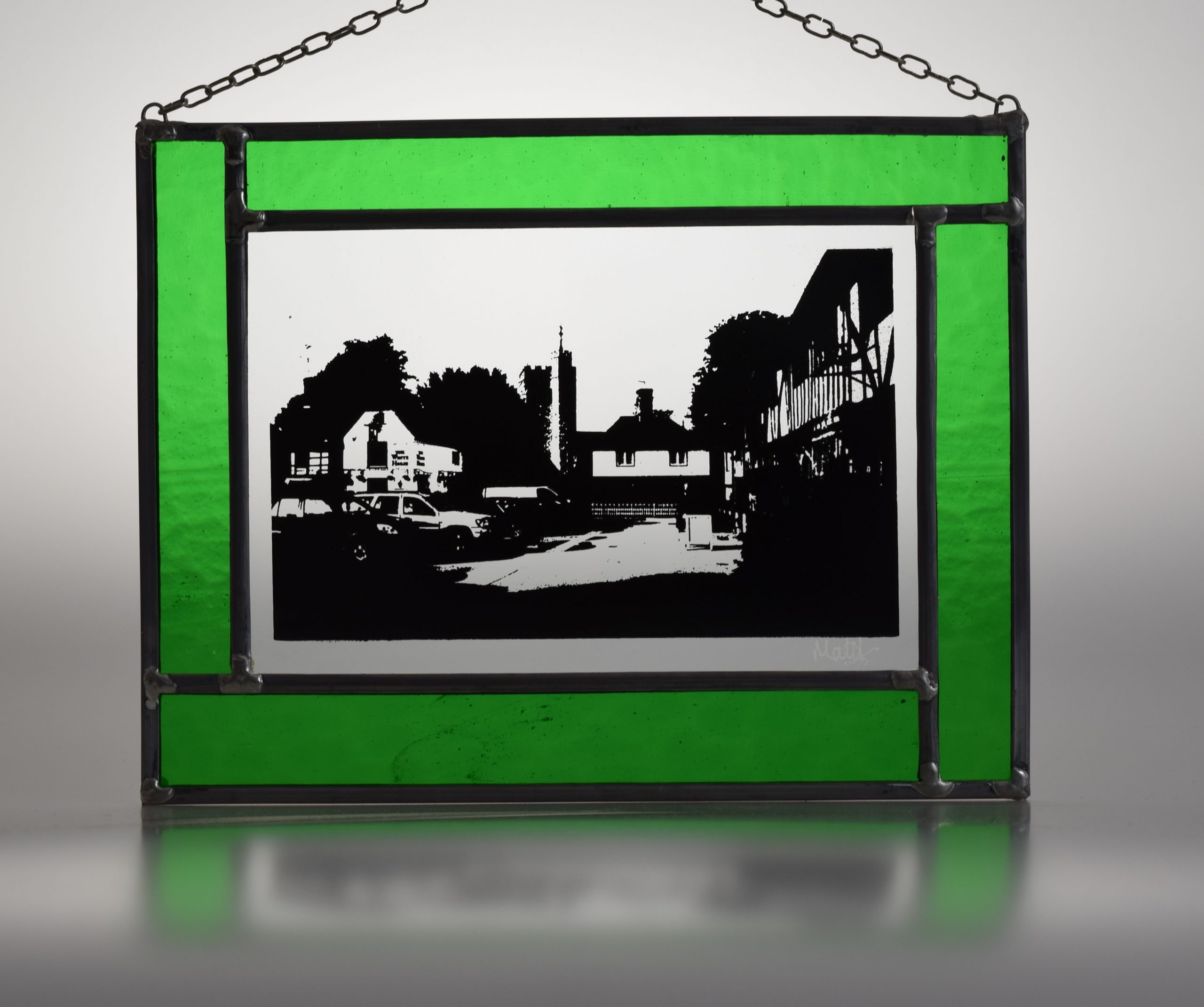 stained glass picture of historic Chilham in a leafy green glass surround