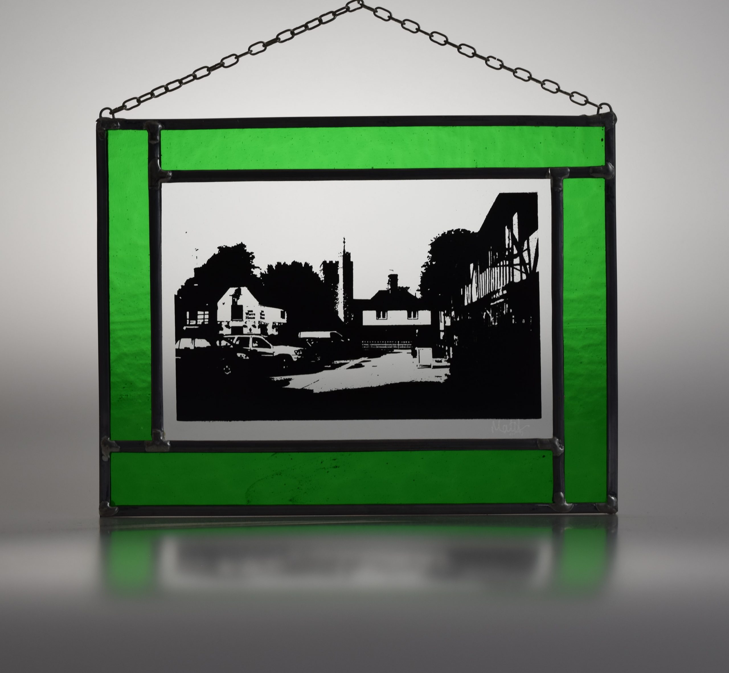 stained glass picture of historic Chilham in a leafy green glass surround