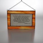 An attractive stained glass panel bearing the words from Jeremiah 29, verses 11 - 13 on white glass, with a glass border in shades of orange and a hanging chain.