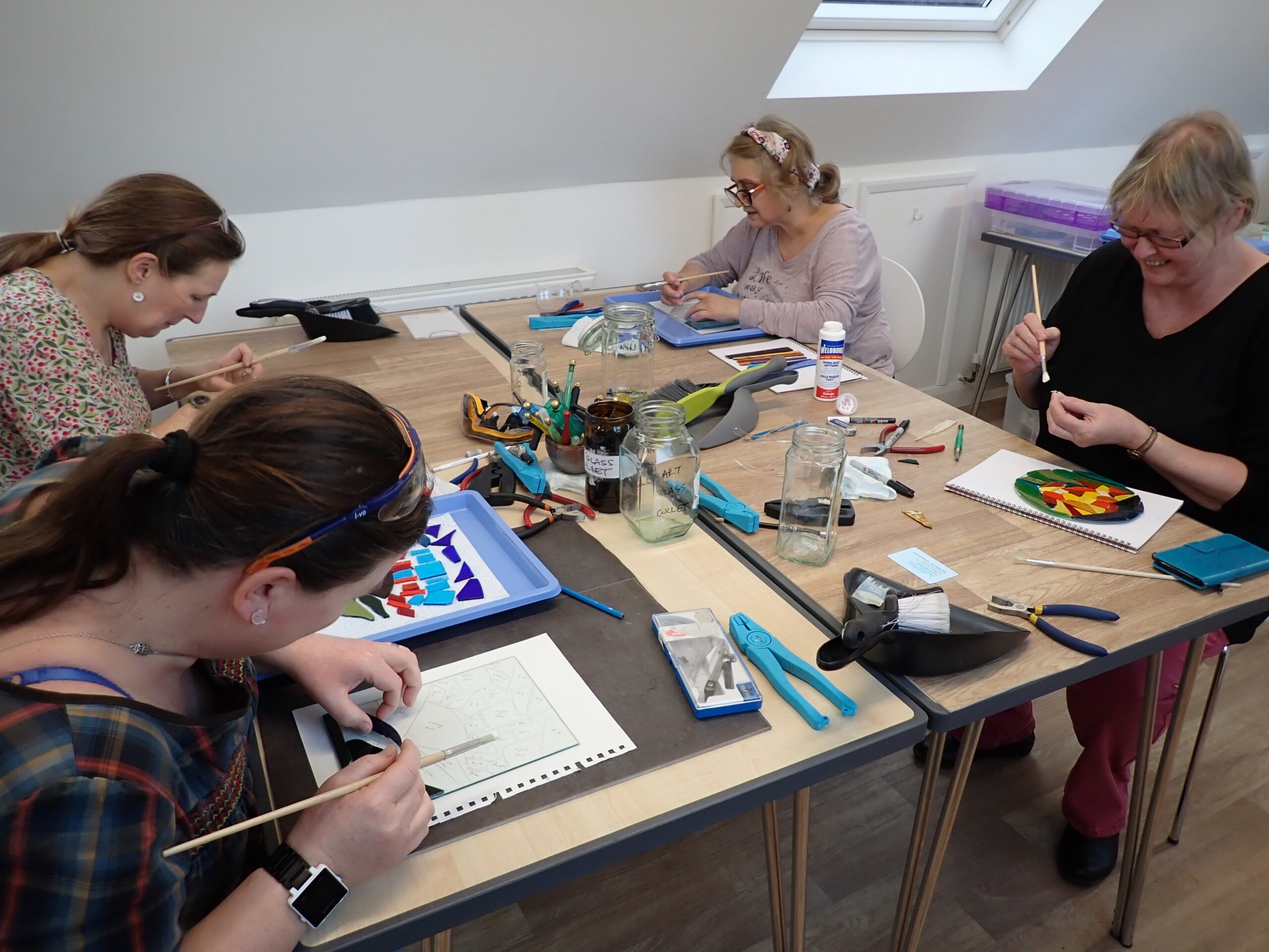 Four visitors to Creative Retreats and Holidays' glass studio glue their stained glass mosaics before finishing them with grout